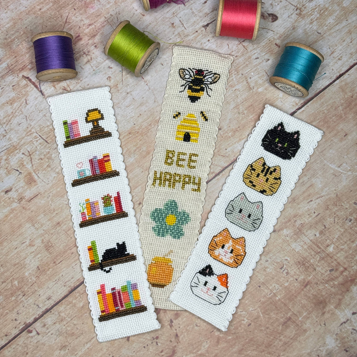 Book Lover Cross Stitch Bookmark Kit displayed with bee and cat cross stitch bookmarks and colourful sewing threads