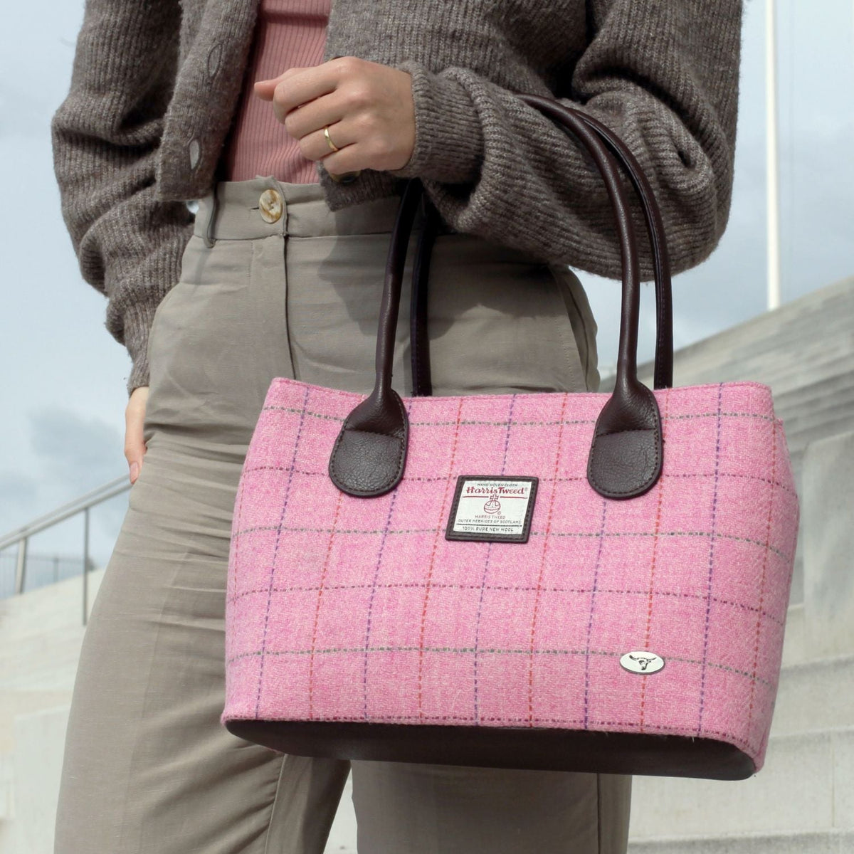Glen Appin Cassley Harris Tweed handbag in pink check with dark brown handles, shown being carried by a model.