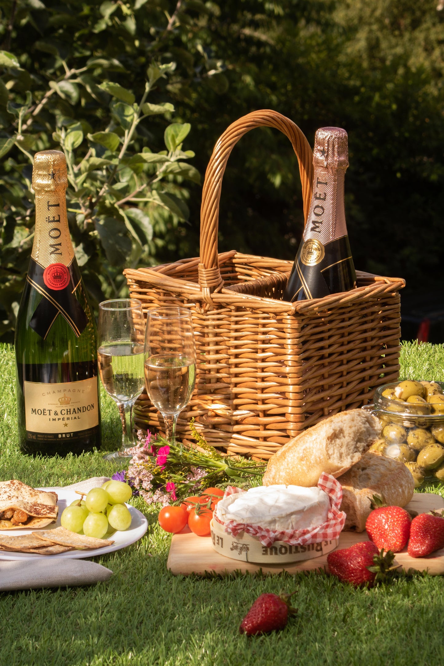 2 bottle willow wine carrier holding bottles in an outdoor picnic setting with food and a wicker picnic basket.