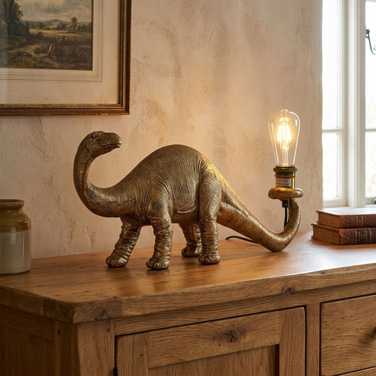 Antique gold Brontosaurus table lamp with glowing exposed bulb displayed on a rustic oak chest.