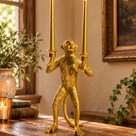 Antique gold standing monkey candelabra with two lit taper candles displayed on a characterful rustic oak console.