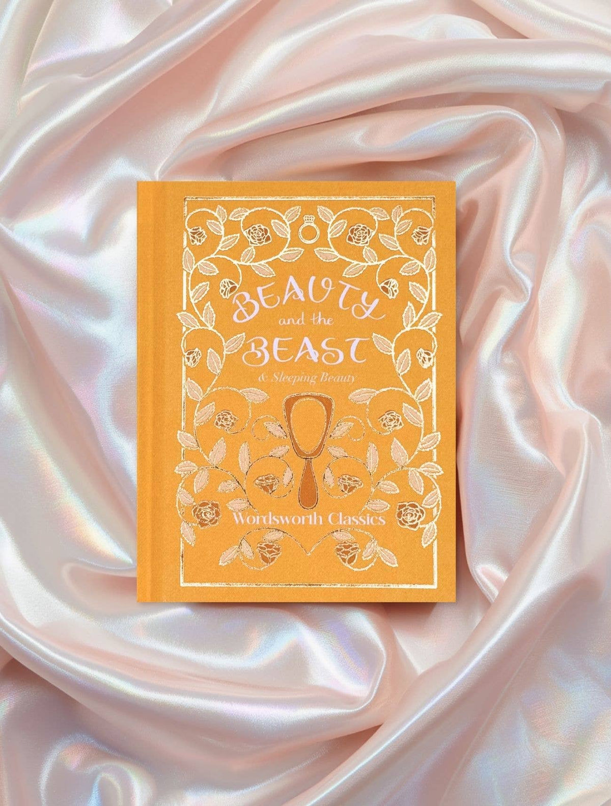 Beauty and the Beast Wordsworth Pocket Fairytales edition with orange illustrated cover displayed on pale pink satin fabric