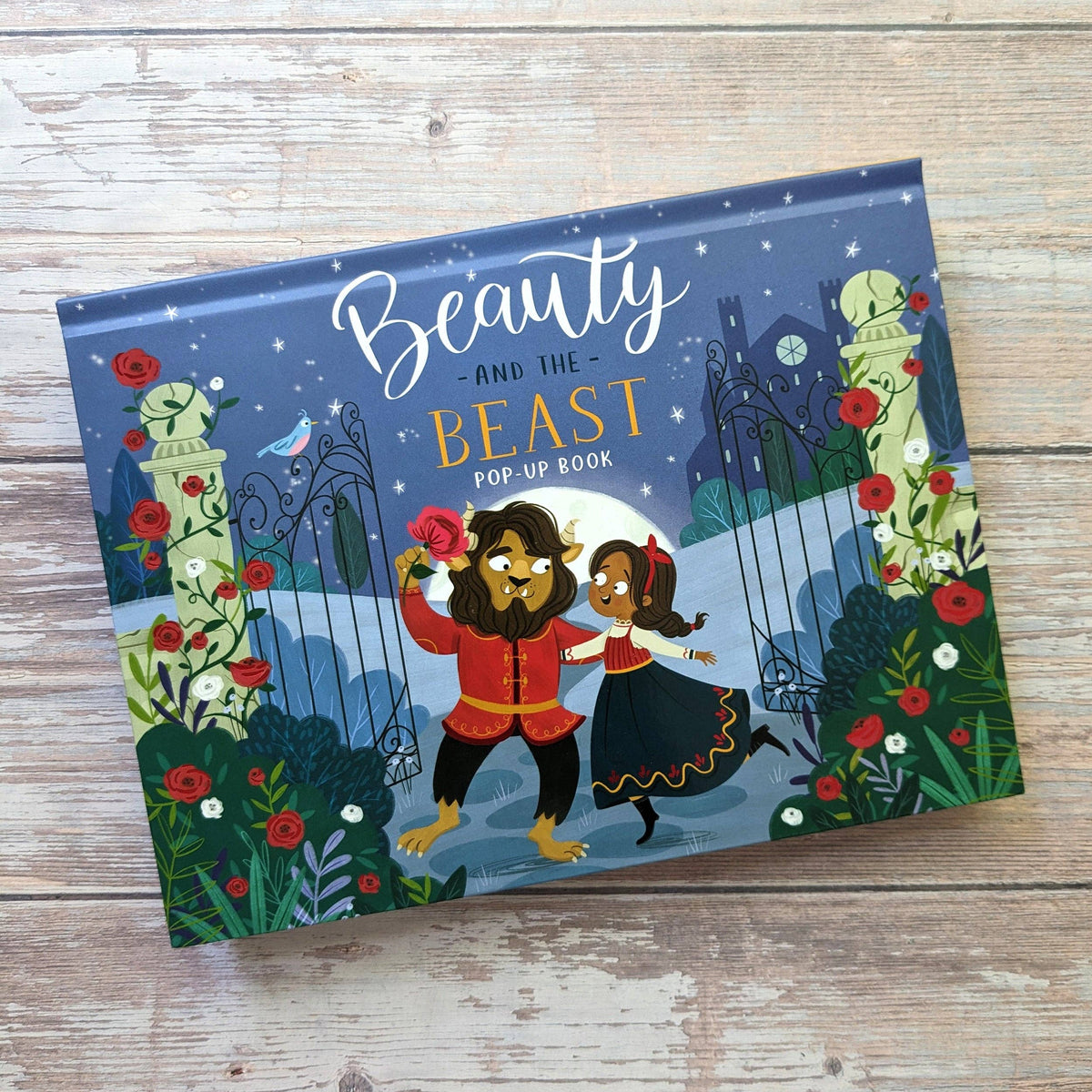 Beauty and the Beast children's pop-up book showing its illustrated front cover on a rustic wooden surface