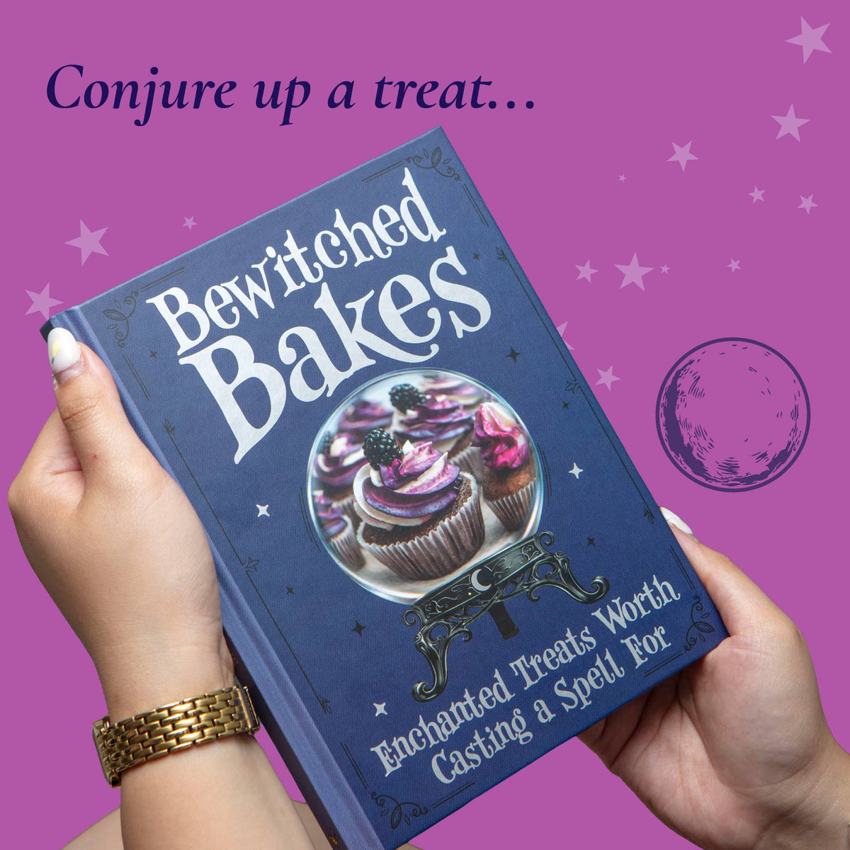 Bewitched Bakes hardback baking book held in the hands, showing its illustrated front cover against a purple background.