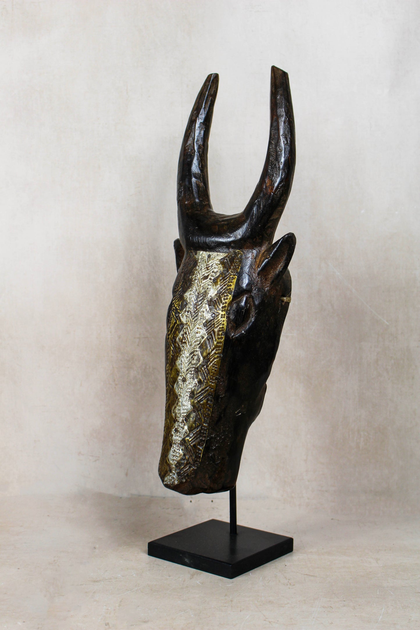 Mali bull mask 196.4 viewed at an angle showing the geometric repoussé metalwork and aged wooden form
