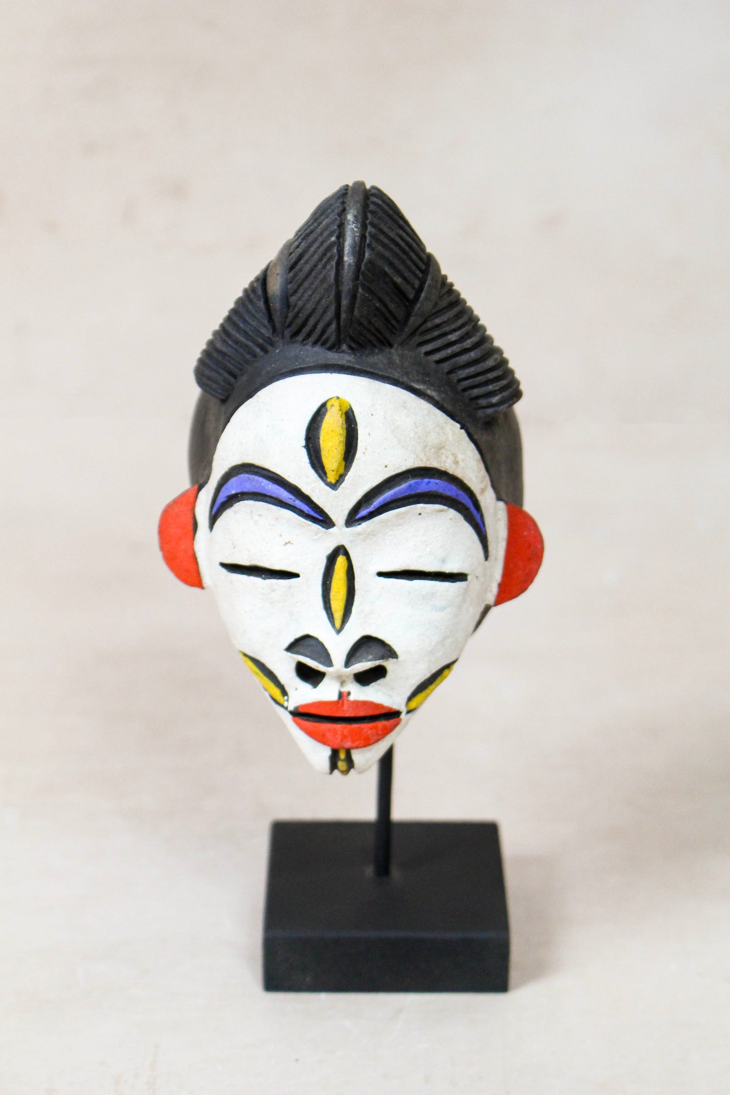 West African terracotta passport mask 189.2 with colourful painted facial details displayed on a black stand
