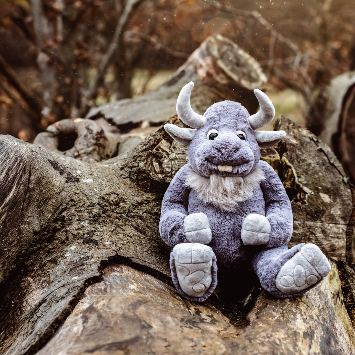 Charlie Bears Cobblestone grey plush giant seated on a fallen tree in a woodland setting