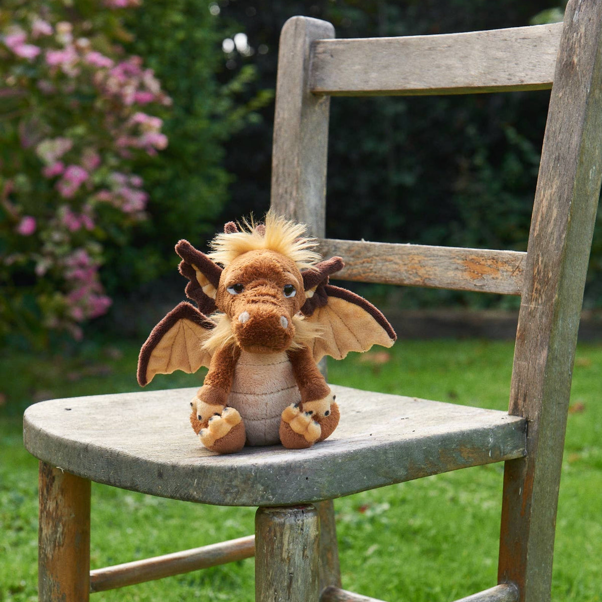 Charlie Bears Cuddle Cub Lantern brown plush dragon sitting on a garden chair