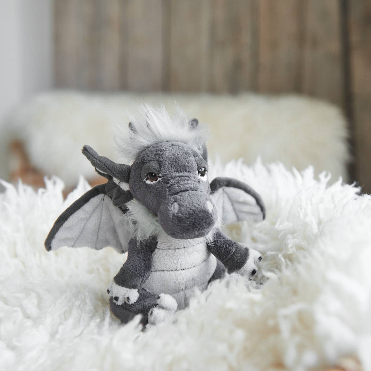 Charlie Bears Cuddle Cub Soot grey plush dragon in a cosy soft setting