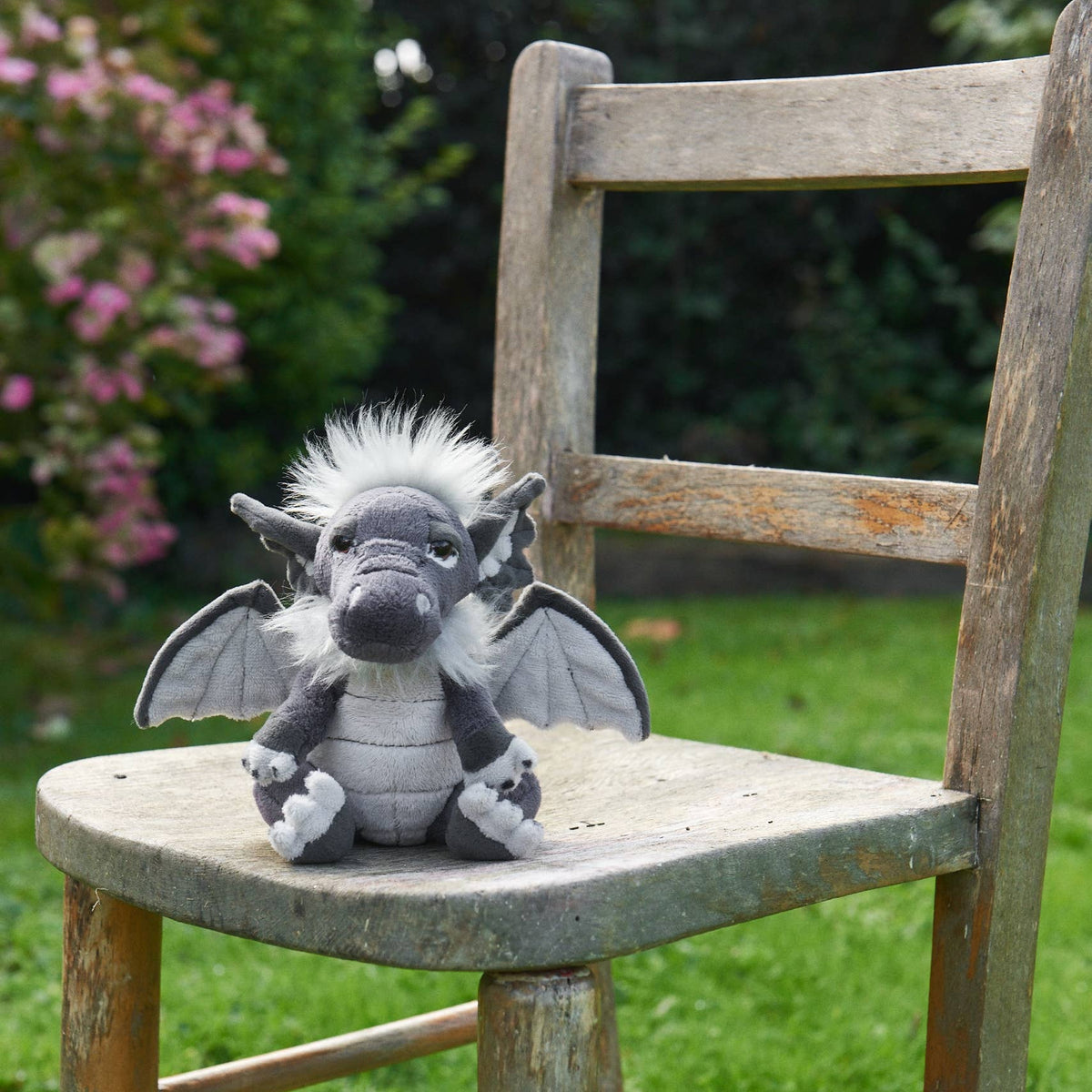 Charlie Bears Cuddle Cub Soot grey plush dragon sitting on a garden chair