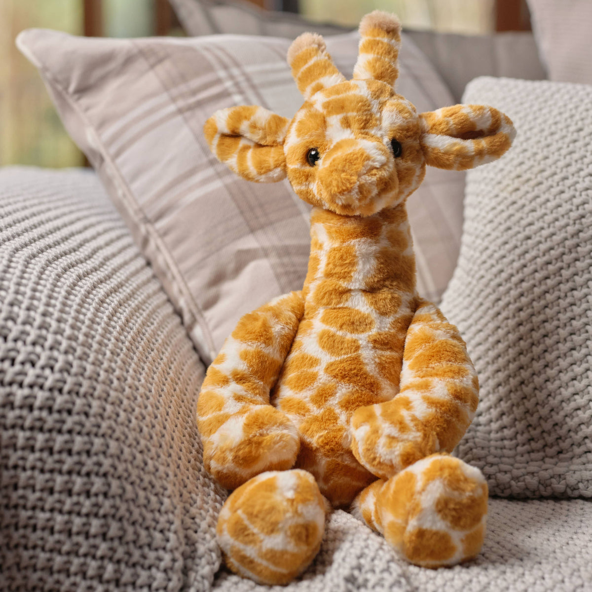 Charlie Bears Gilbert Giraffe plush soft toy sitting on a neutral sofa