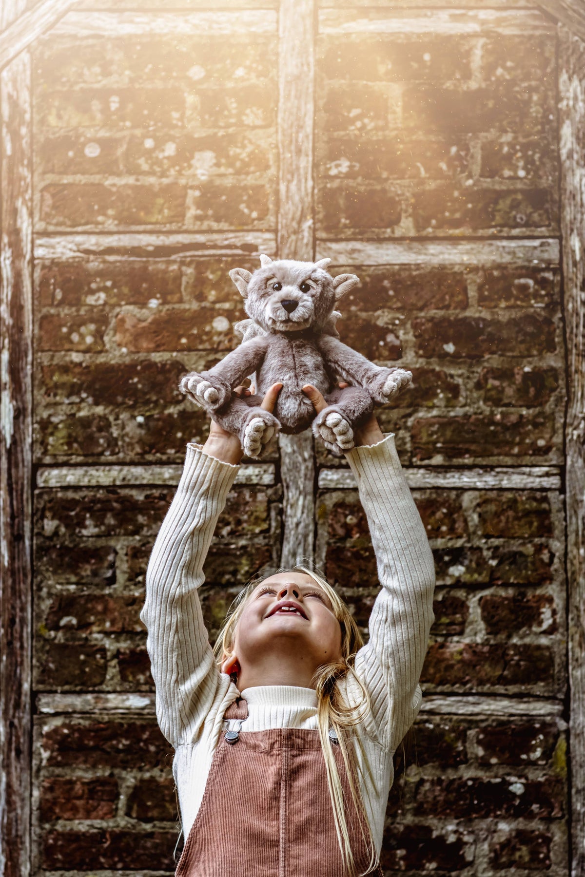 Charlie Bears Moat grey plush gargoyle being held outdoors against a rustic stone wall