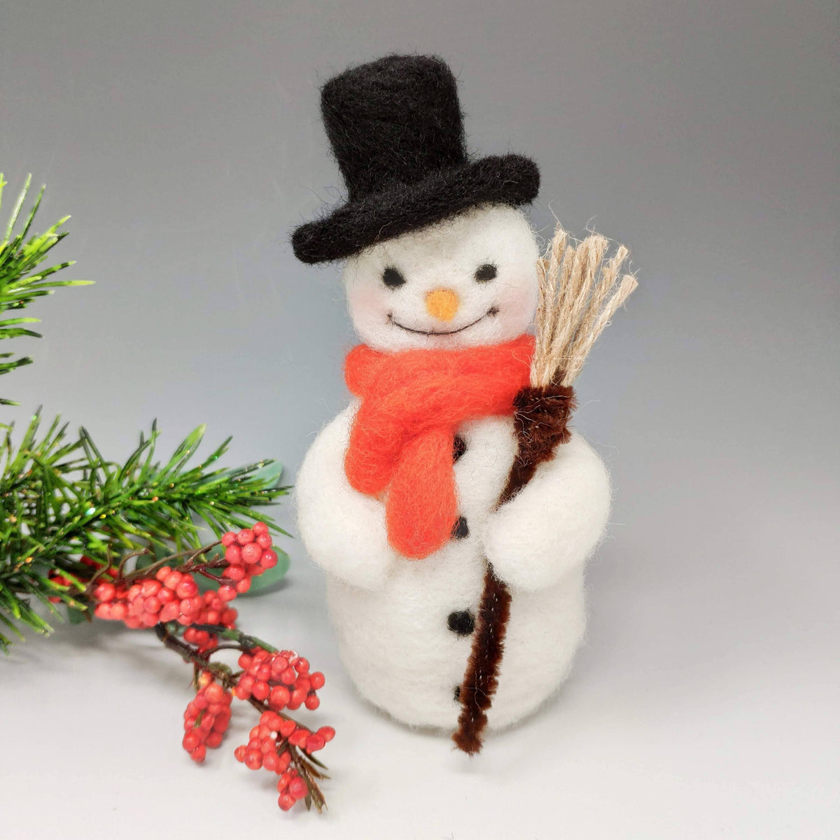 Festive Snowman Needle Felting Craft Kit finished wool snowman with black top hat, red scarf and broom beside Christmas greenery