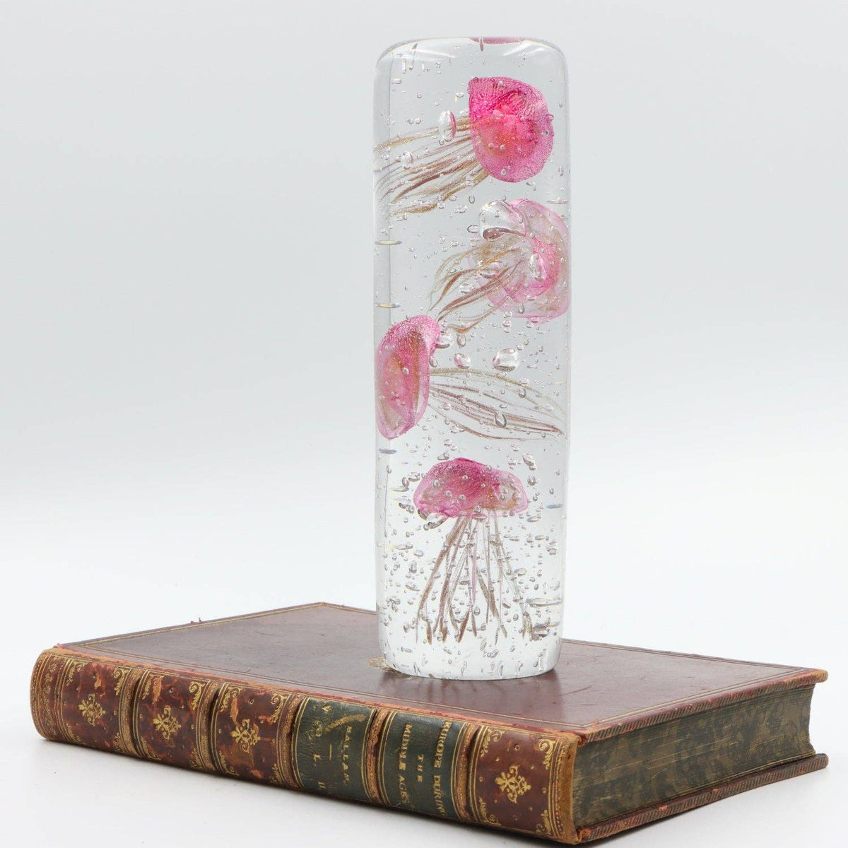 Four Pink Jellyfish glass paperweight displayed upright on a vintage book
