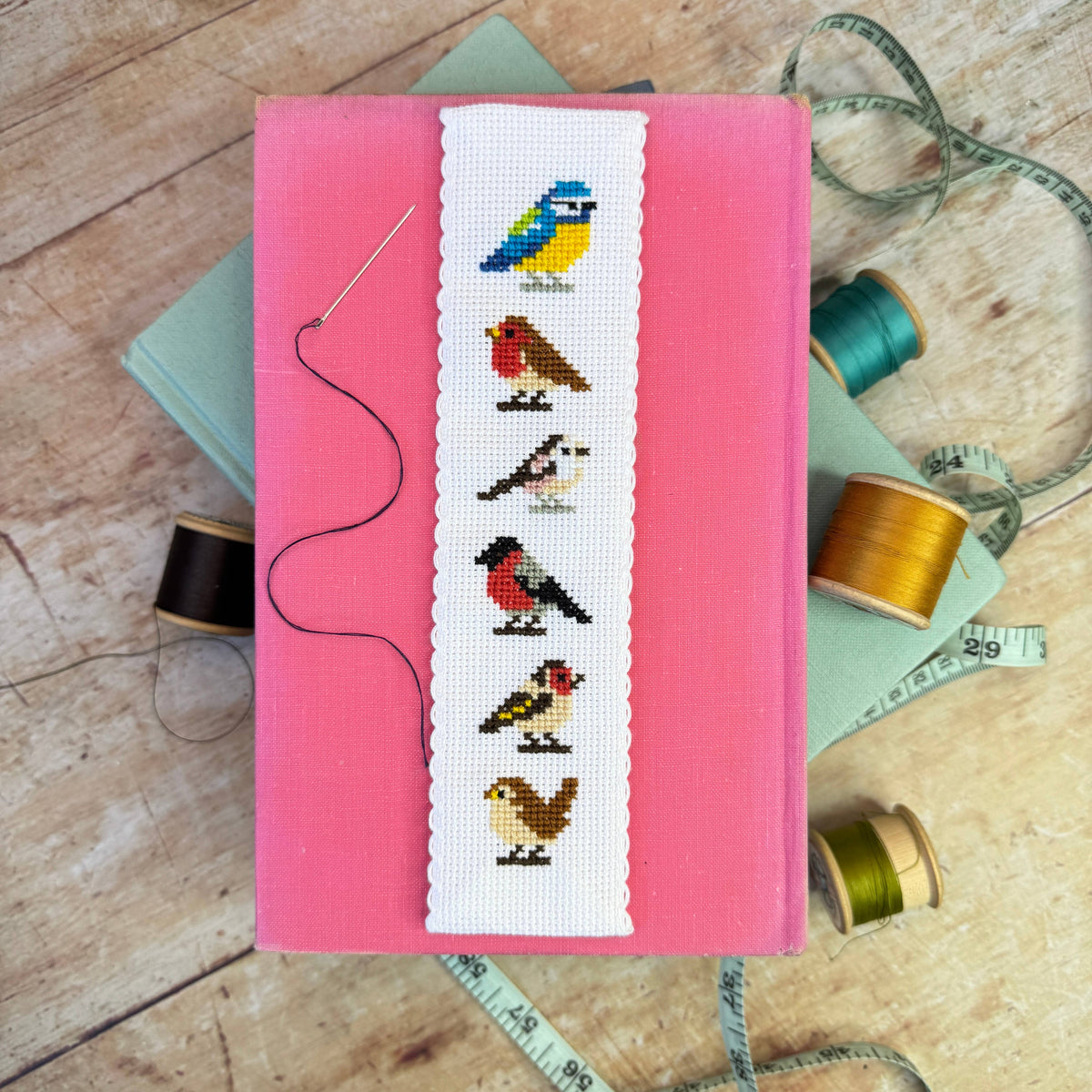 Garden Birds Cross Stitch Bookmark Kit finished bird bookmark styled on a pink book with colourful sewing threads