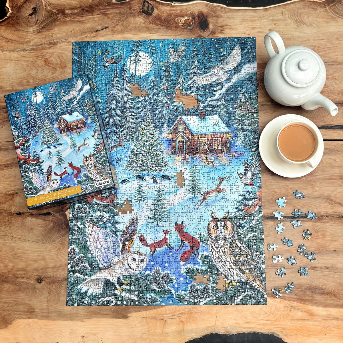 Dancing in the Moonlight 1000 piece jigsaw puzzle by Gibsons, displayed on a rustic wooden table with its box, loose pieces and a cup of tea.