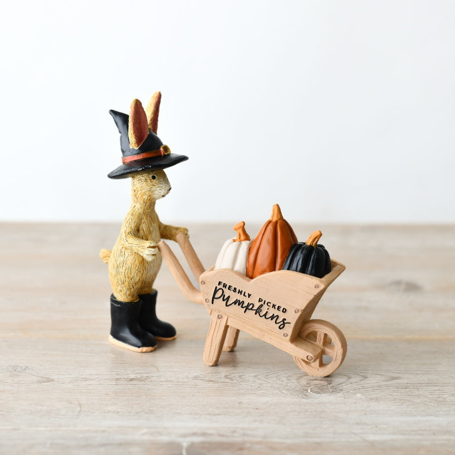 Jasper Rabbit Pumpkin Patch Figure wearing a witch’s hat and pushing a wheelbarrow filled with orange, cream and black pumpkins