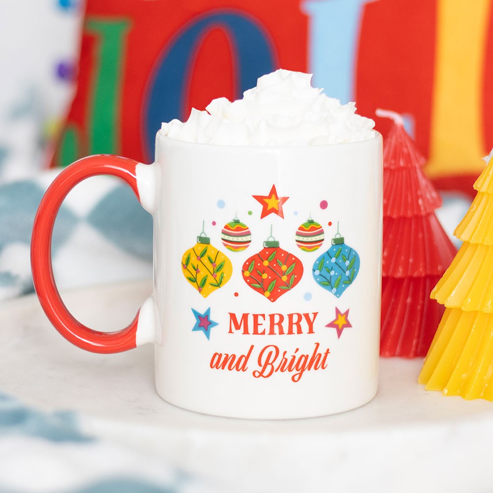 Merry and Bright Christmas Mug with colourful bauble design and red handle, filled with whipped cream in a festive setting