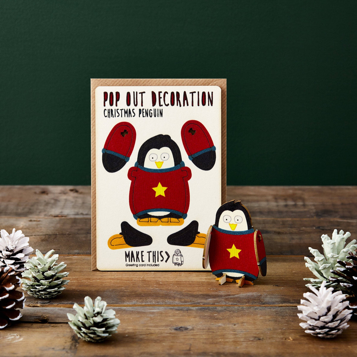 Pop Out Penguin Christmas Card with assembled festive penguin in a red and teal jumper displayed in a Christmas setting