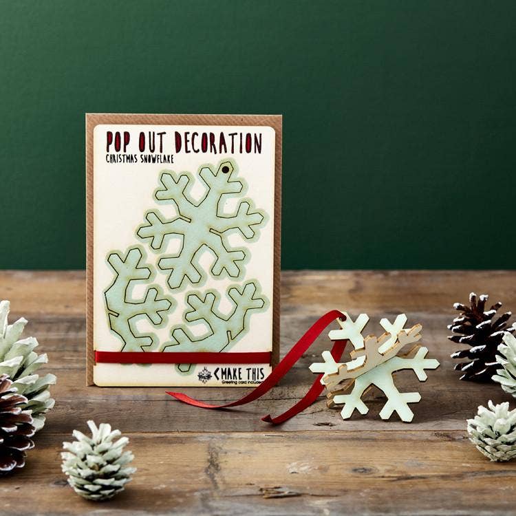 Pop Out Snowflake Christmas Card with assembled pale blue wooden snowflake decoration and red hanging ribbon in a festive setting