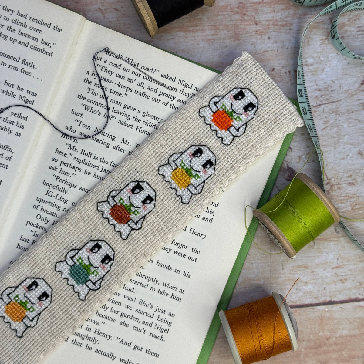 Pumpkin Ghosts Cross Stitch Bookmark Kit finished embroidered ghost bookmark marking the pages of an open book