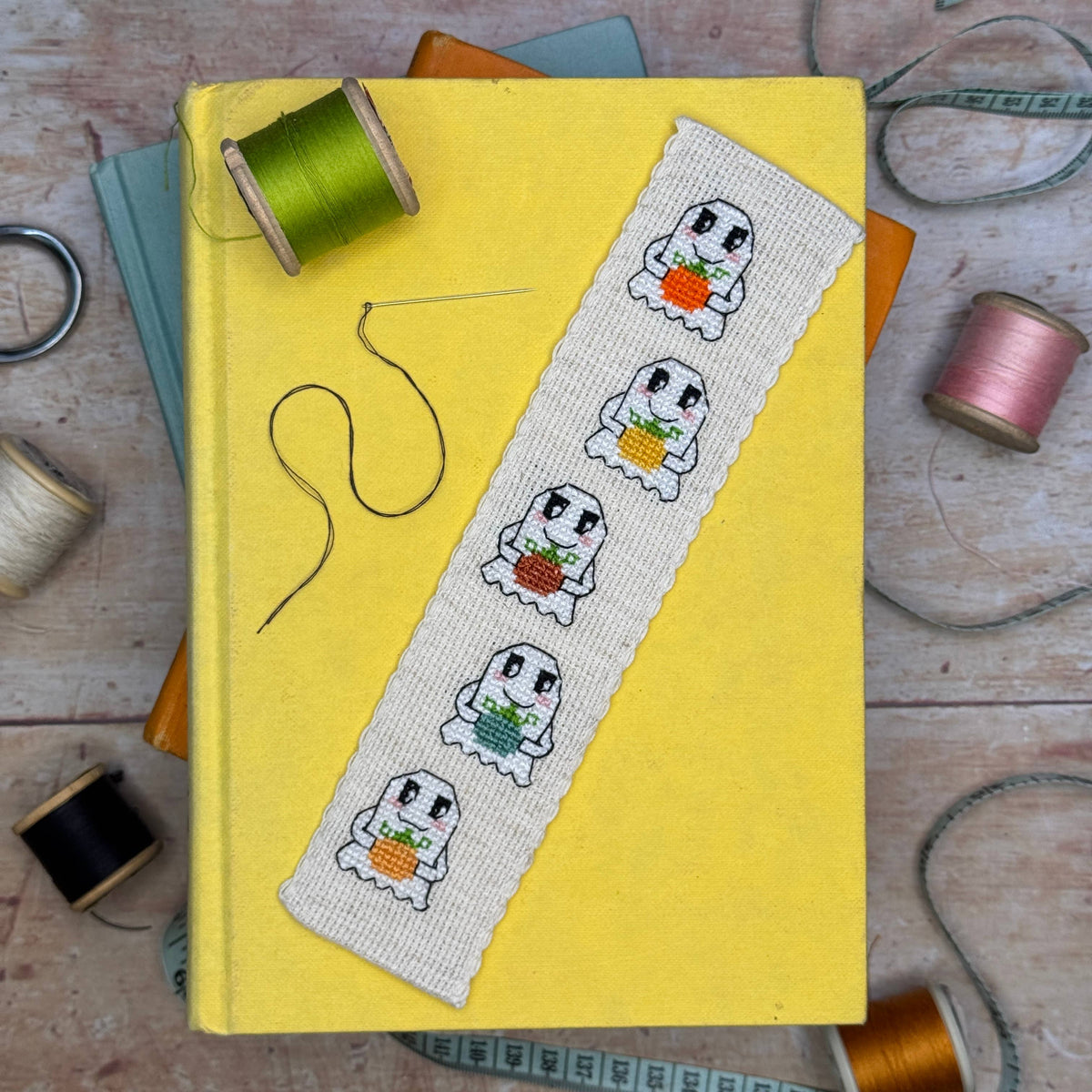 Pumpkin Ghosts Cross Stitch Bookmark Kit finished ghost bookmark styled on a yellow book with colourful sewing threads