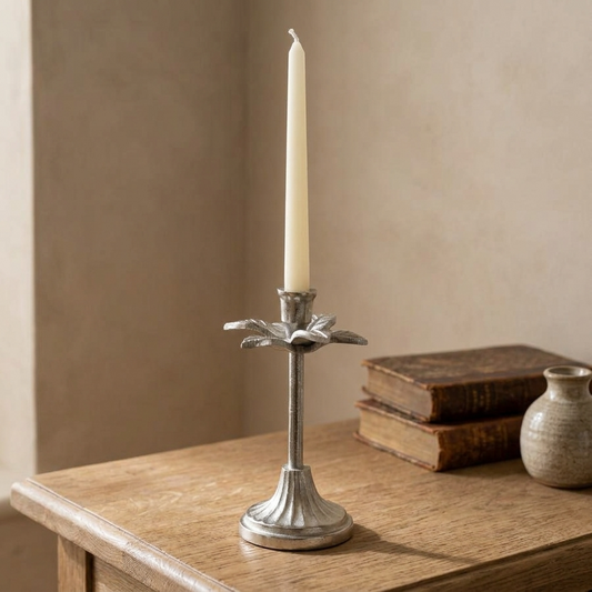 Silver leaf candlestick with an ivory taper candle displayed on a rustic oak table against a warm neutral wall.