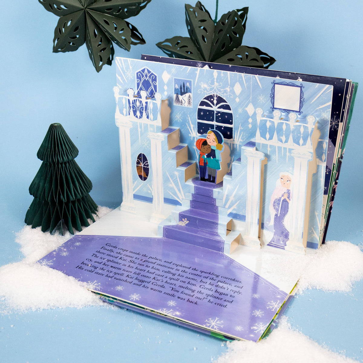 The Snow Queen children's pop-up book opened against a pale blue background, showing its detailed winter pop-up illustrations