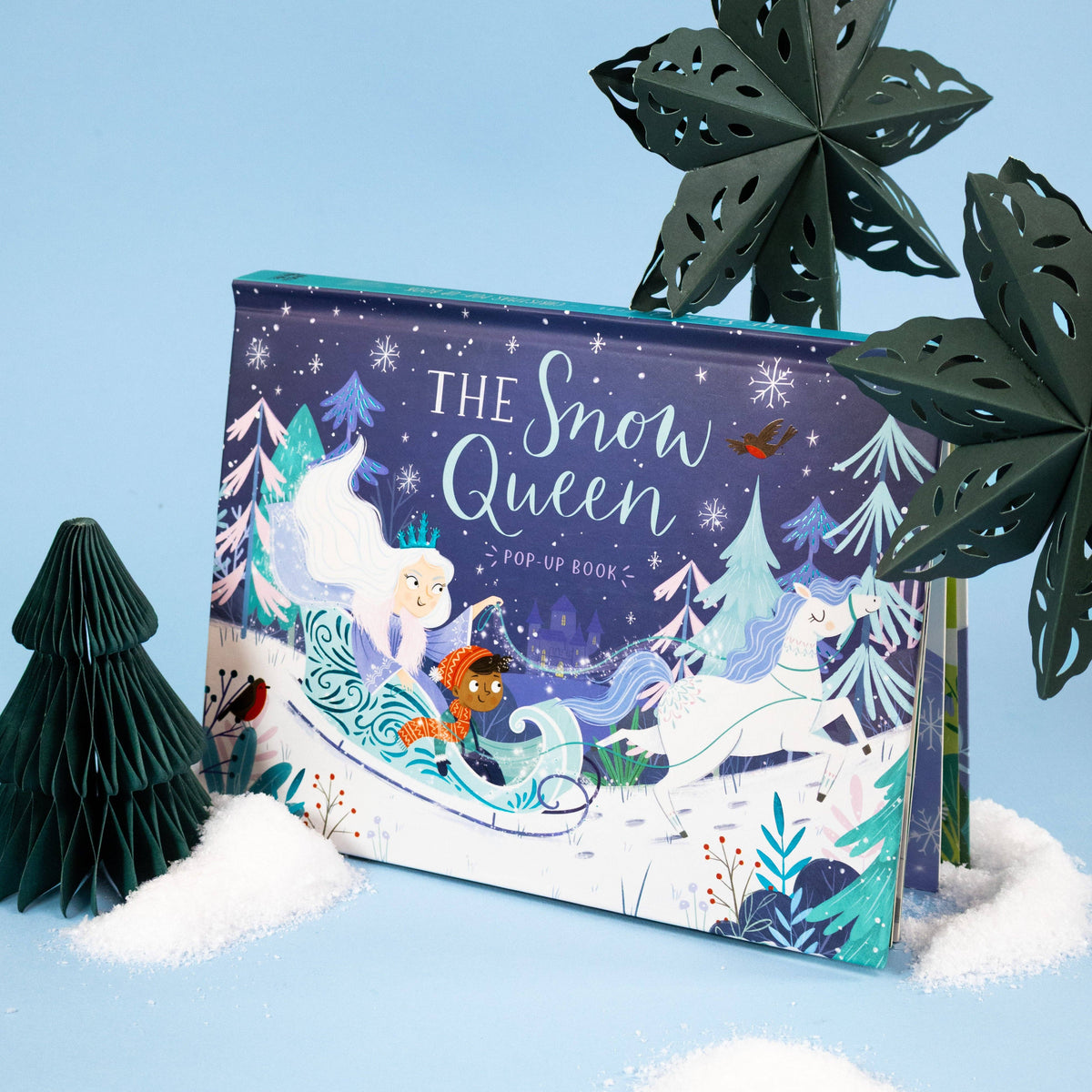 The Snow Queen pop-up book photographed against a pale blue winter-themed background with decorative trees